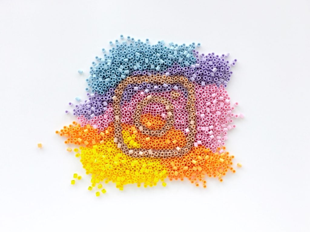 Instagram logo made of rainbow coloured pyssla beads blue purple pink orange yellow white background